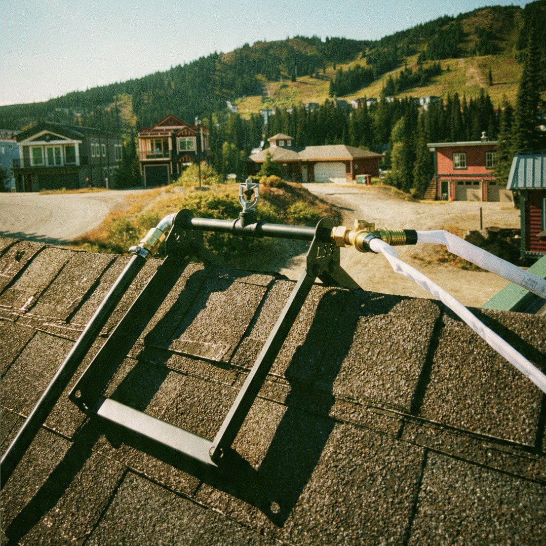 Ridge-mount sprinkler manifold and supply hose installed on a mountain-side home roof