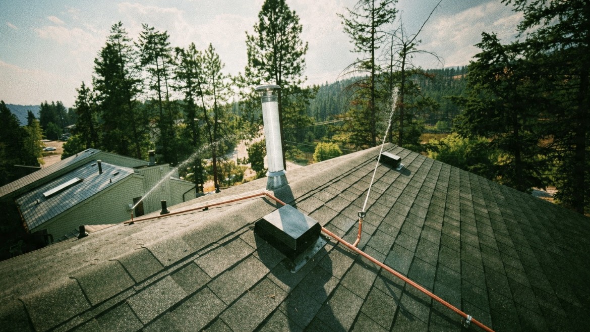 Rooftop wildfire sprinkler system spraying water across a shingled Okanagan roof