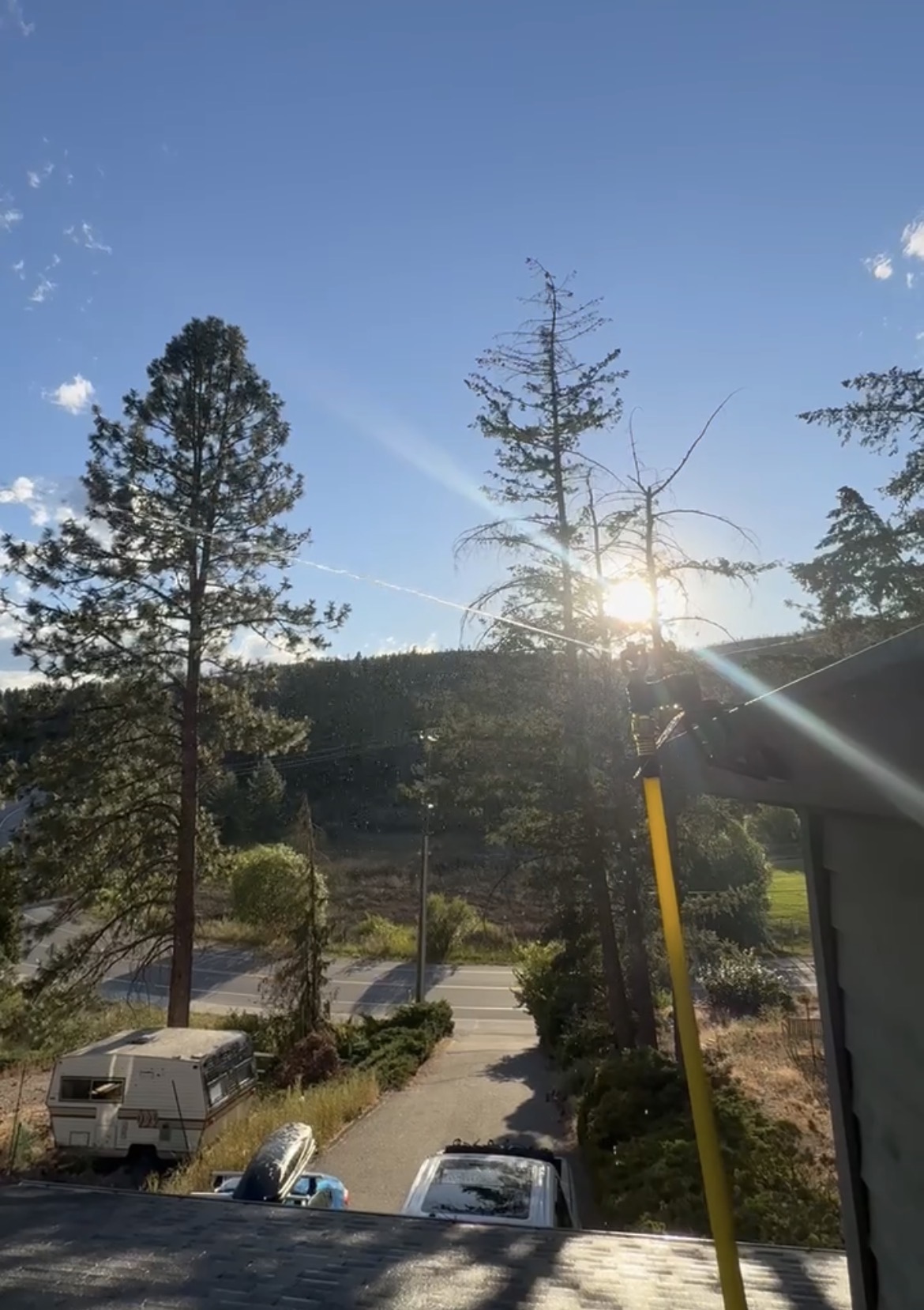 Wildfire sprinkler spraying from rooftop pole at sunset over Okanagan property